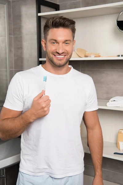 Hombre alegre en camiseta blanca sosteniendo cepillo de dientes en el baño - foto de stock