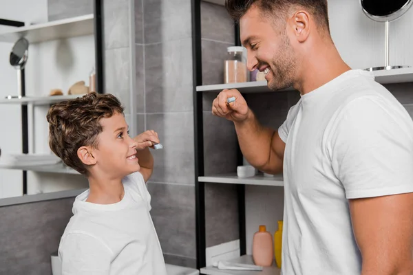 Niño feliz sosteniendo el cepillo de dientes y mirando al padre en el baño - foto de stock