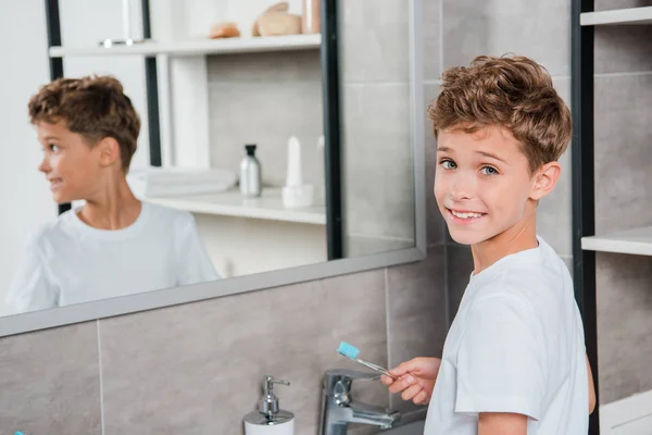 Messa a fuoco selettiva del ragazzo allegro che tiene lo spazzolino in bagno — Foto stock