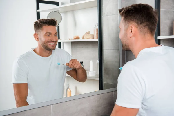 Selective focus of cheerful man holding toothbrush and looking at mirror — Stock Photo