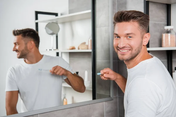 Enfoque selectivo del hombre alegre sosteniendo cepillo de dientes cerca del espejo - foto de stock