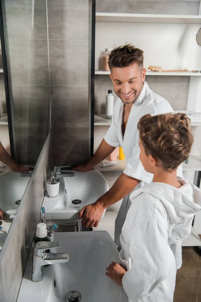 Selective focus of happy father looking at son near bathroom sinks — Stock Photo