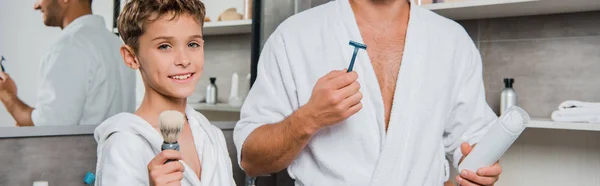 Colpo panoramico di padre tenuta rasoio e può con schiuma da barba vicino figlio felice con pennello da barba — Foto stock