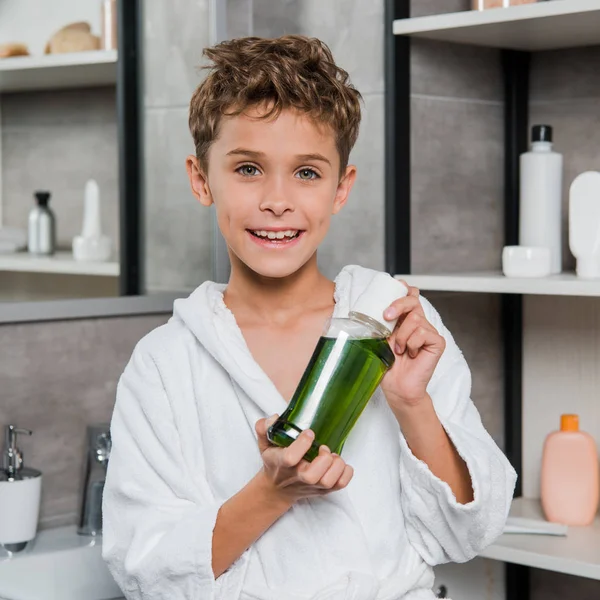 Garçon gai tenant bouteille avec bain de bouche vert dans la salle de bain — Photo de stock