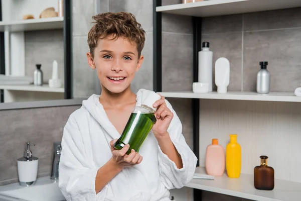 Heureux garçon tenant bouteille avec bain de bouche vert dans la salle de bain — Photo de stock
