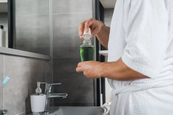 Vista recortada del hombre sosteniendo botella verde con enjuague bucal - foto de stock