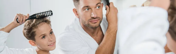 Tiro panorâmico de homem bonito e bonito garoto escovando o cabelo no banheiro — Fotografia de Stock