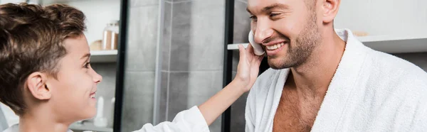 Colpo panoramico di figlio che applica la schiuma da barba a faccia di bambino — Foto stock