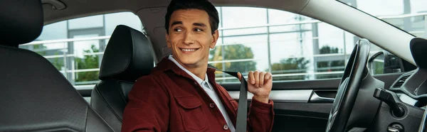 Smiling young man holding safety belt in car, panoramic shot — Stock Photo