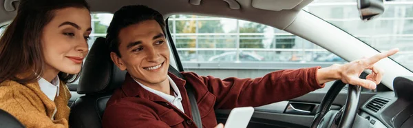 Passenger looking at smartphone while taxi driver pointing on road, panoramic shot — Stock Photo