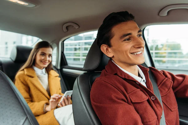 Selektiver Fokus lächelnder Taxifahrer und Frau mit Smartphone im Auto — Stockfoto