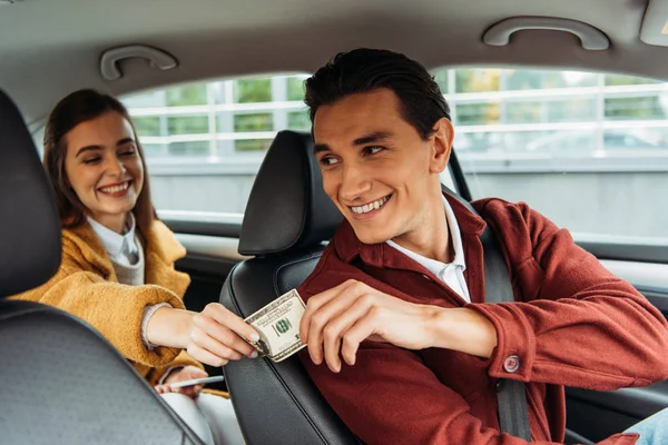 Jeune femme passager donnant de l'argent au chauffeur de taxi souriant — Photo de stock