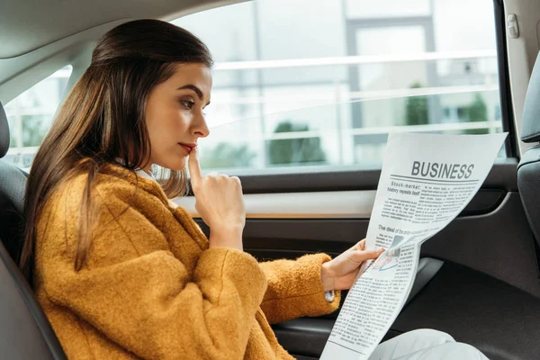 Mujer joven pensativa leyendo el periódico en el asiento trasero del taxi - foto de stock