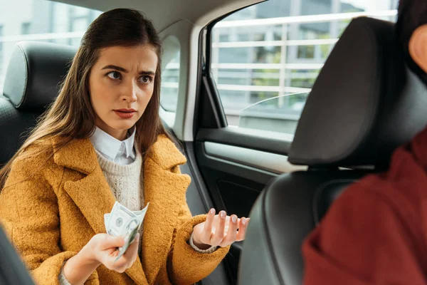 Giovane donna scontenta in possesso di contanti e guardando il conducente in taxi — Foto stock