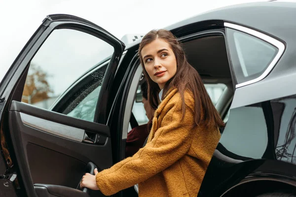 Young woman getting out of taxi and looking away — Stock Photo