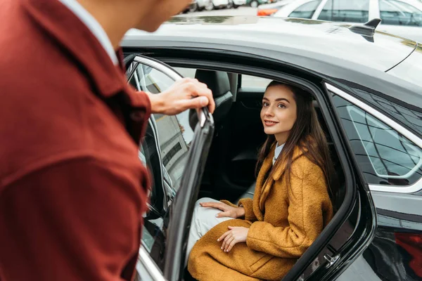 Sobre a vista do ombro do motorista de táxi que abre a porta do carro para a mulher — Fotografia de Stock