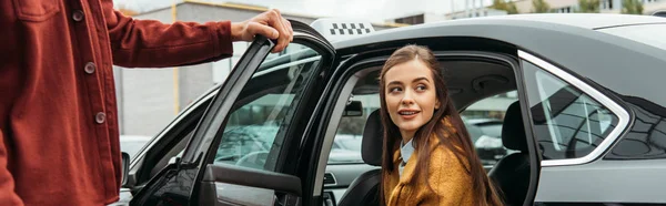 Taxi conductor abriendo la puerta del coche para la mujer sonriente, tiro panorámico - foto de stock