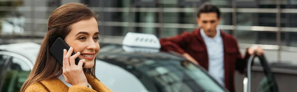 Selective focus of woman talking on smartphone and taxi driver at background, panoramic shot — Stock Photo