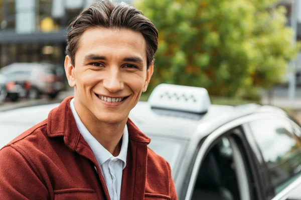 Foco seletivo de homem sorridente com táxi em segundo plano — Fotografia de Stock