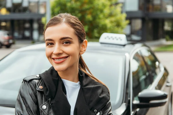 Усміхнена жінка таксист дивиться на камеру біля машини — стокове фото