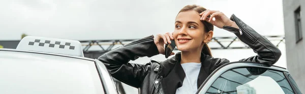 Mujer sonriente taxista hablando en el teléfono inteligente al lado del coche, tiro panorámico - foto de stock