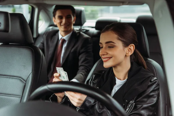 Chauffeur de taxi souriant tenant de l'argent comptant avec un homme d'affaires en arrière-plan — Photo de stock