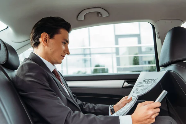 Businessman holding newspaper and smartphone in taxi — Stock Photo