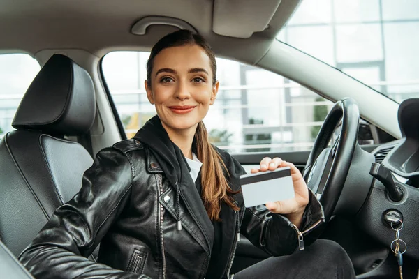 Mujer sosteniendo tarjeta de crédito y sonriendo a la cámara en el coche - foto de stock