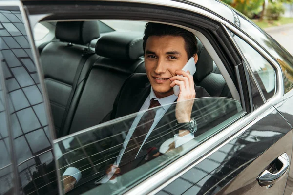 Улыбающийся бизнесмен разговаривает по смартфону на заднем сиденье такси — стоковое фото