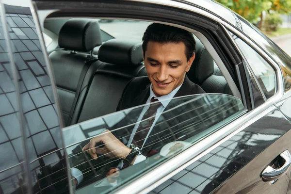 Hombre de negocios sonriente mirando reloj de pulsera en taxi - foto de stock