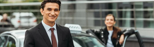 Enfoque selectivo de sonriente hombre de negocios y taxista en coche, plano panorámico - foto de stock