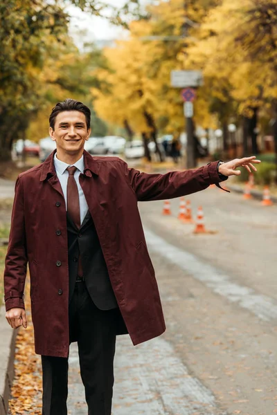 Un hombre de negocios sonriente cogiendo un taxi en la calle durante el otoño - foto de stock