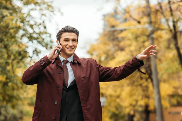 Smiling businessman catching taxi and talking on smartphone — Stock Photo