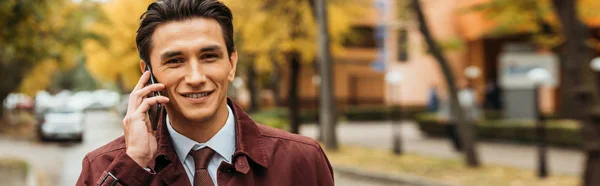 Homme d'affaires souriant parlant sur smartphone dans la rue, panoramique — Photo de stock