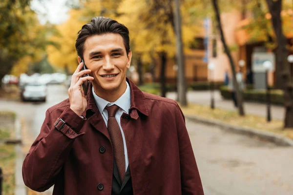 Lächelnder Geschäftsmann, der auf der Straße mit dem Smartphone spricht — Stockfoto