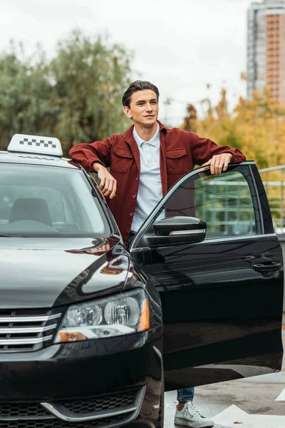 Taxi driver guardando altrove accanto alla porta dell'auto aperta — Foto stock