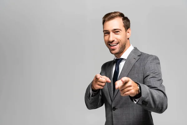 Hombre de negocios sonriente y guapo en traje señalando con los dedos aislados en gris - foto de stock