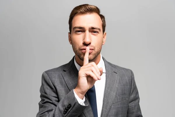 Handsome businessman in suit showing shh sign isolated on grey — Stock Photo