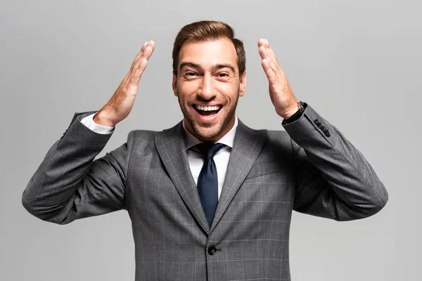 Handsome and smiling businessman in suit looking at camera isolated on grey — Stock Photo