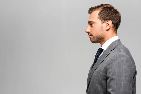 Vista lateral del hombre de negocios guapo en traje aislado en gris - foto de stock