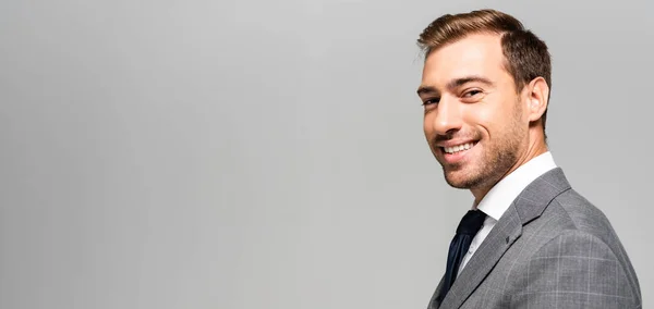 Panoramic shot of smiling and handsome businessman in suit looking at camera isolated on grey — Stock Photo