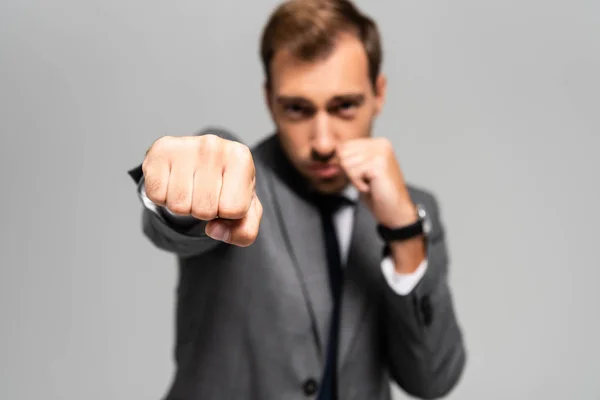 Selective focus of handsome businessman in suit punching isolated on grey — Stock Photo
