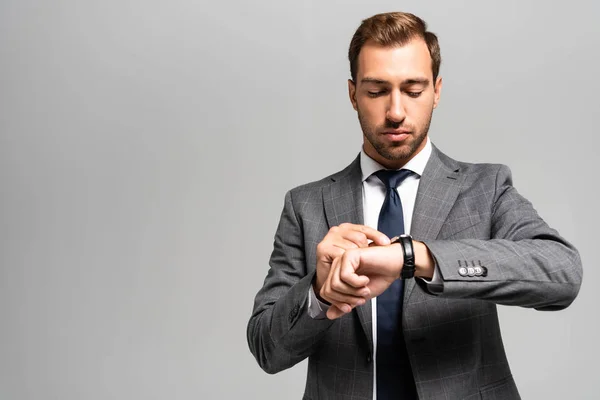 Schöner Geschäftsmann im Anzug schaut auf Armbanduhr isoliert auf grau — Stockfoto