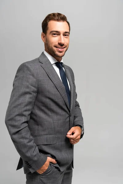 Gutaussehender und lächelnder Geschäftsmann im Anzug, der in die Kamera schaut, isoliert auf grau — Stockfoto