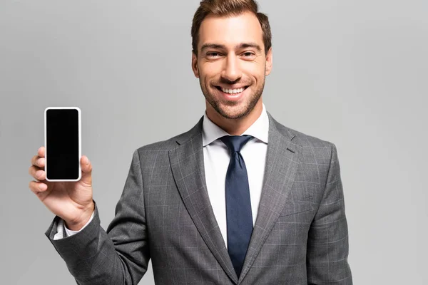 Gutaussehender und lächelnder Geschäftsmann im Anzug, Smartphone isoliert auf grau — Stockfoto