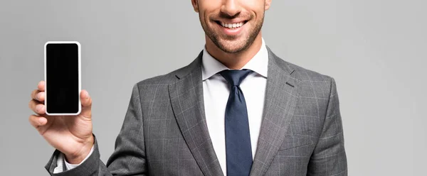 Plano panorámico de hombre de negocios sonriente en traje con teléfono inteligente aislado en gris - foto de stock