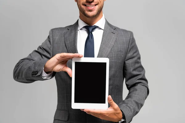 Обрізаний вид усміхненого бізнесмена в костюмі, що тримає цифровий планшет ізольований на сірому — стокове фото