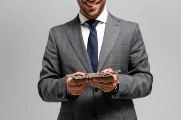 Cropped view of smiling businessman in suit holding dollar banknotes isolated on grey — Stock Photo