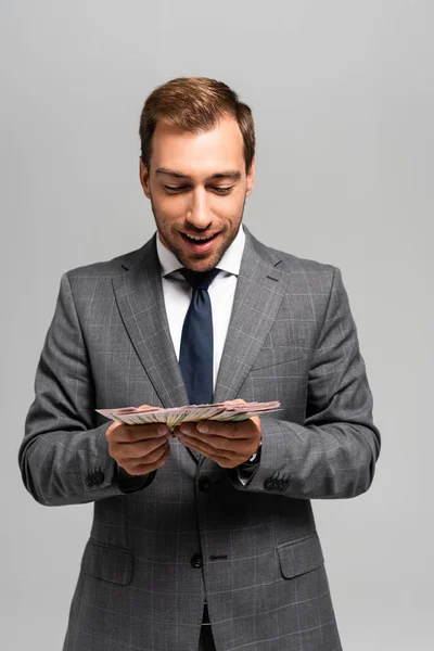 Homme d'affaires beau et souriant en costume tenant des billets en dollars isolés sur gris — Photo de stock