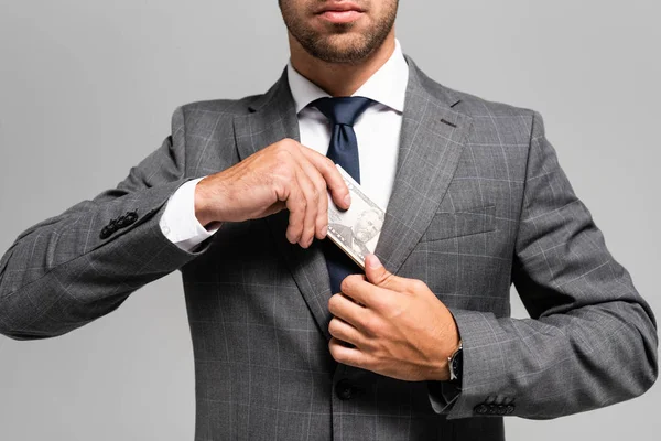 Vista recortada del hombre de negocios en traje ocultando billetes de dólar aislados en gris - foto de stock